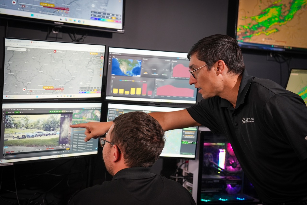 Two security team members sit at stations in a Robotic Security Operations Center in front of large video monitors. 