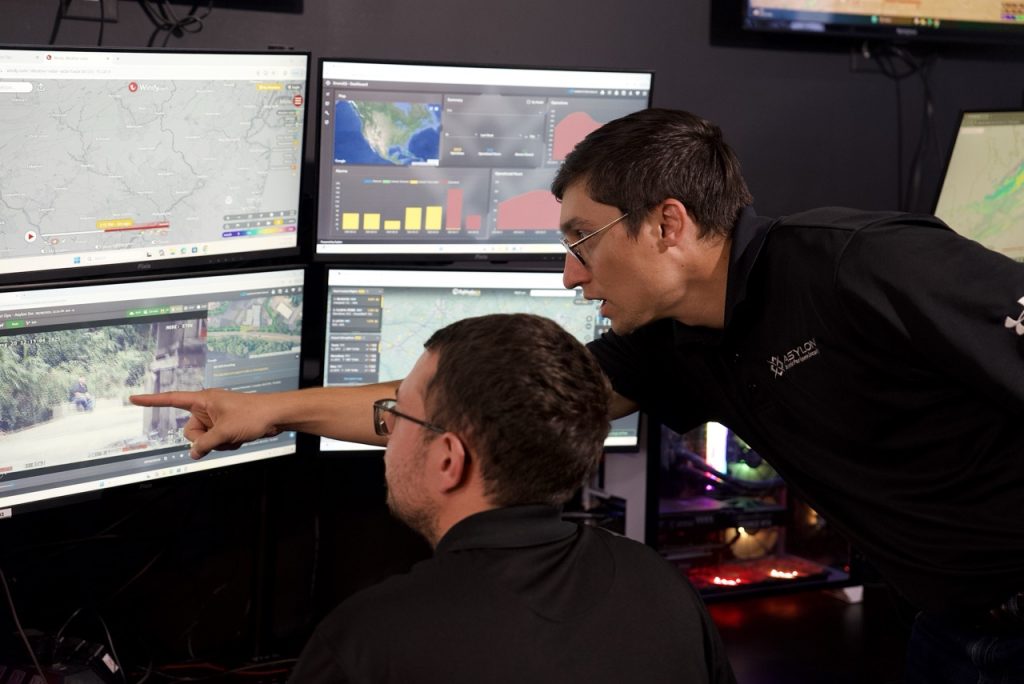 Two security operators review live drone footage and site data on multiple monitors inside Asylon’s robotic security operations center.