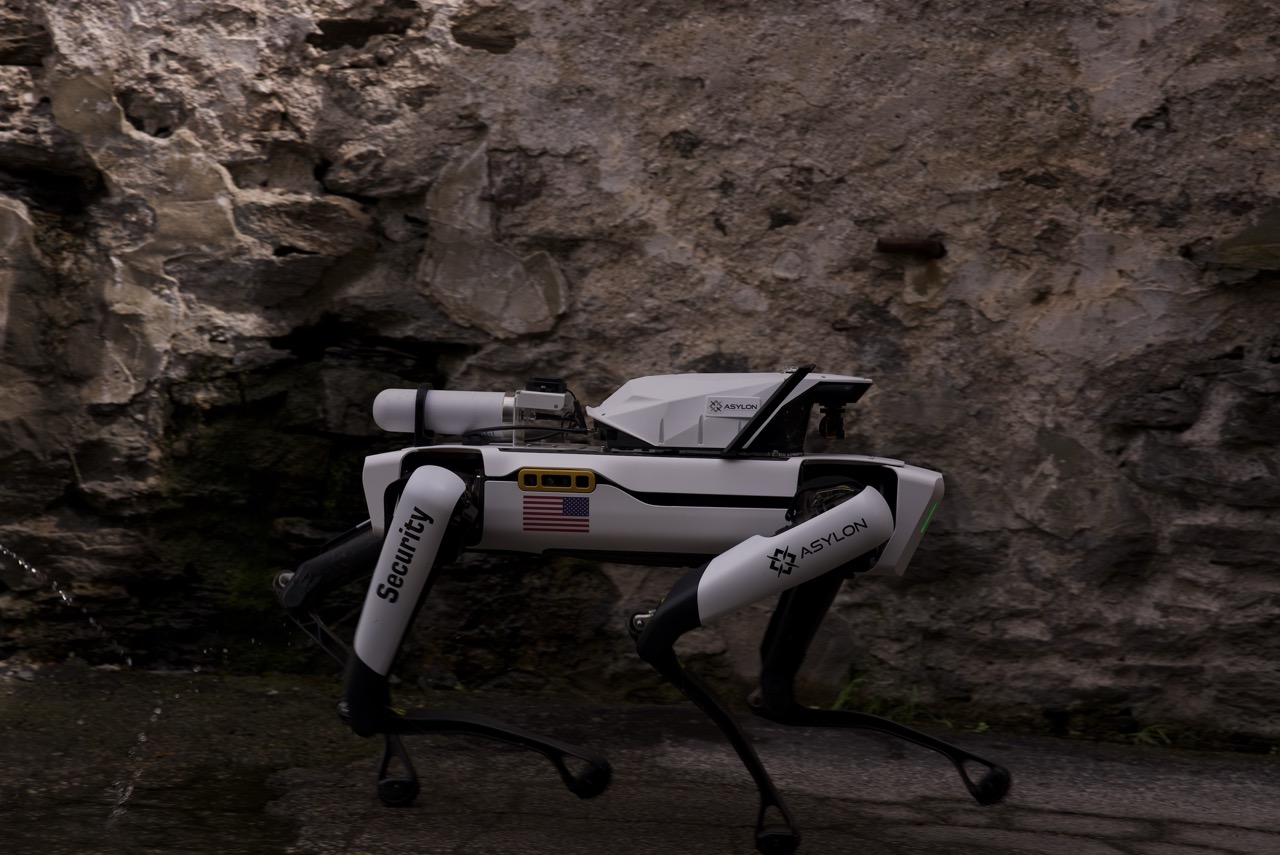 DroneDog security robot from Asylon Robotics patrols a stone wall on a corporate campus.