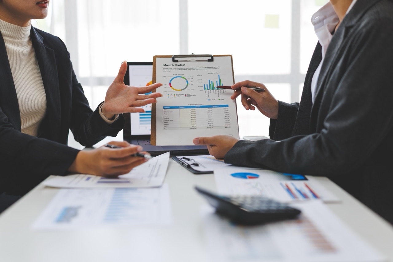 Two members of a corporate board of directors sit at a conference table, reviewing security expenses on a monthly budget report.