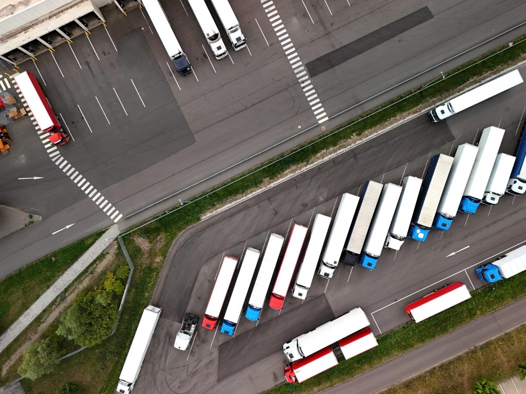Aerial drone view of semi-trucks parked across a large logistics yard and gate area.