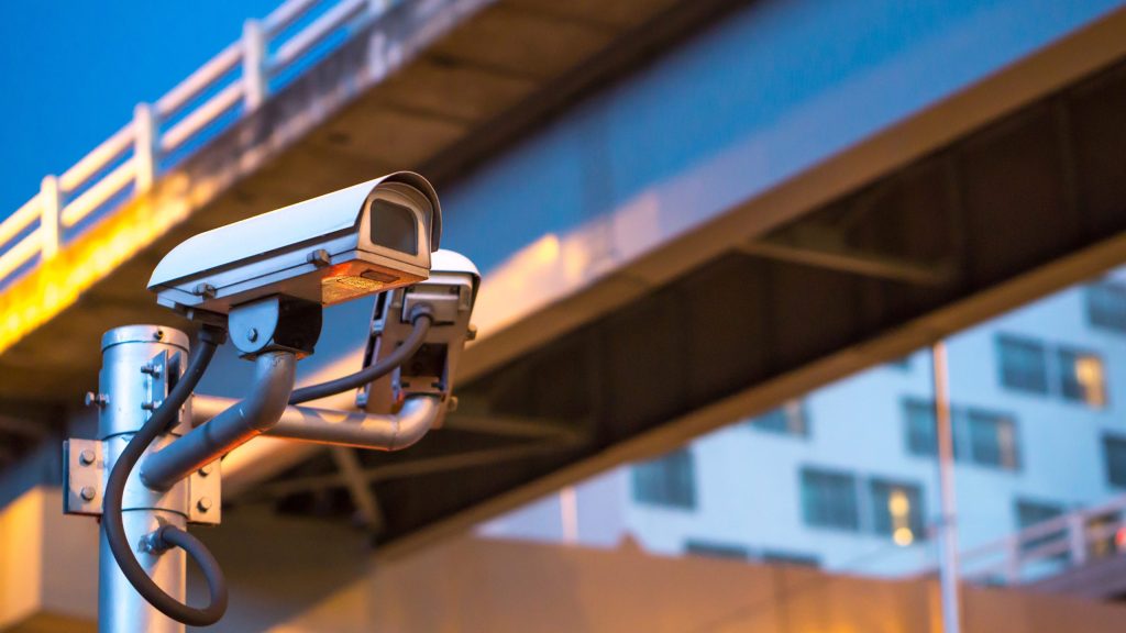 Fixed security camera mounted near a roadway, showing static CCTV coverage limitations.