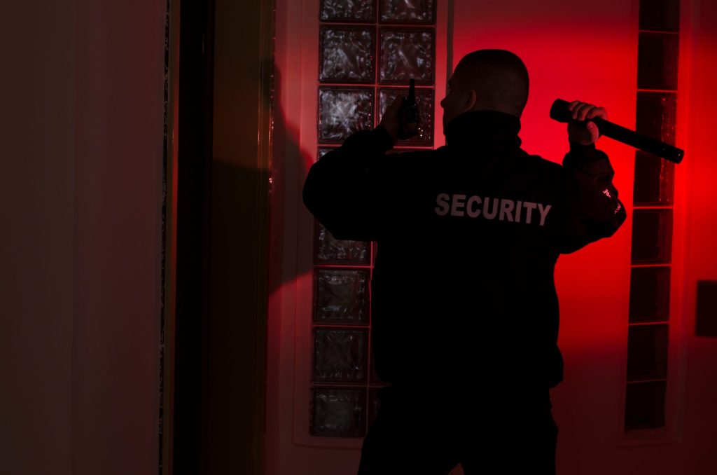 Security officer uses a flashlight while checking a building entrance at night.