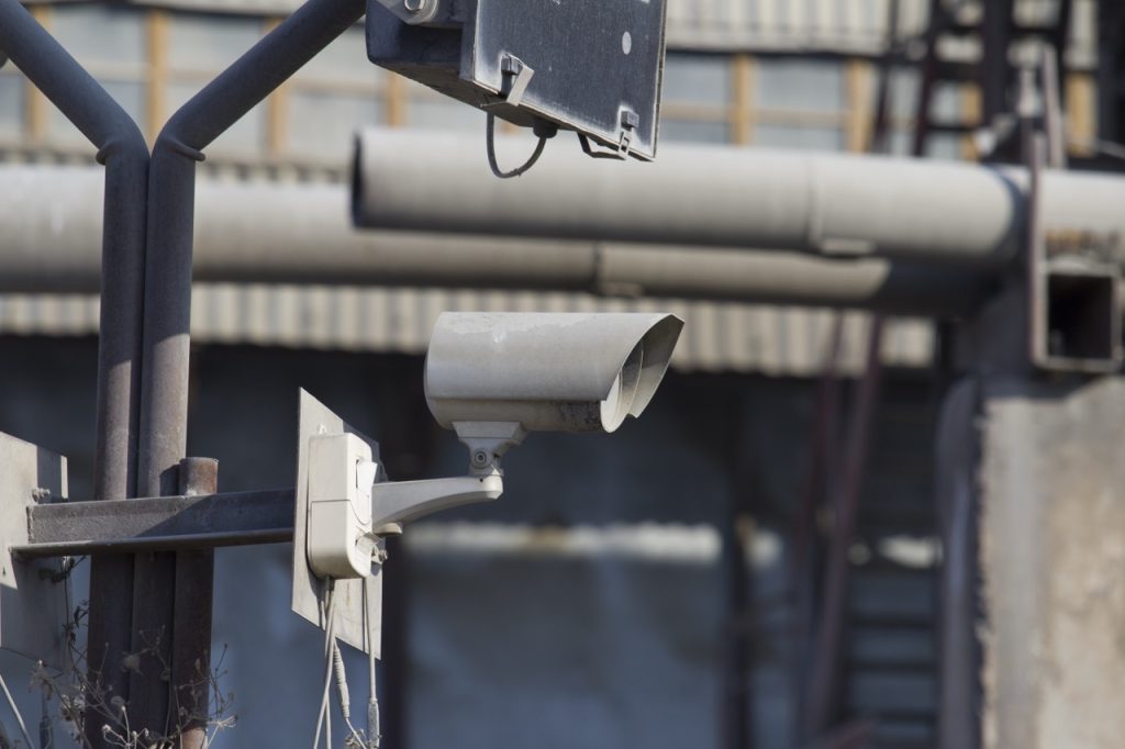 Security camera mounted on a pole monitoring an industrial manufacturing facility perimeter. 