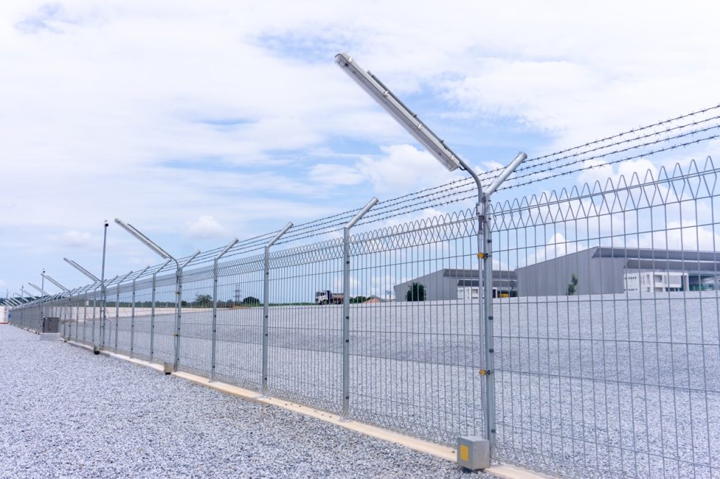Security fence surrounding an industrial manufacturing facility with a large open perimeter area. 