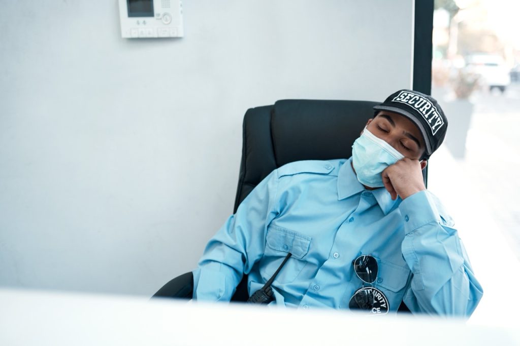Security guard asleep at a monitoring desk, highlighting challenges with overnight security coverage. 
