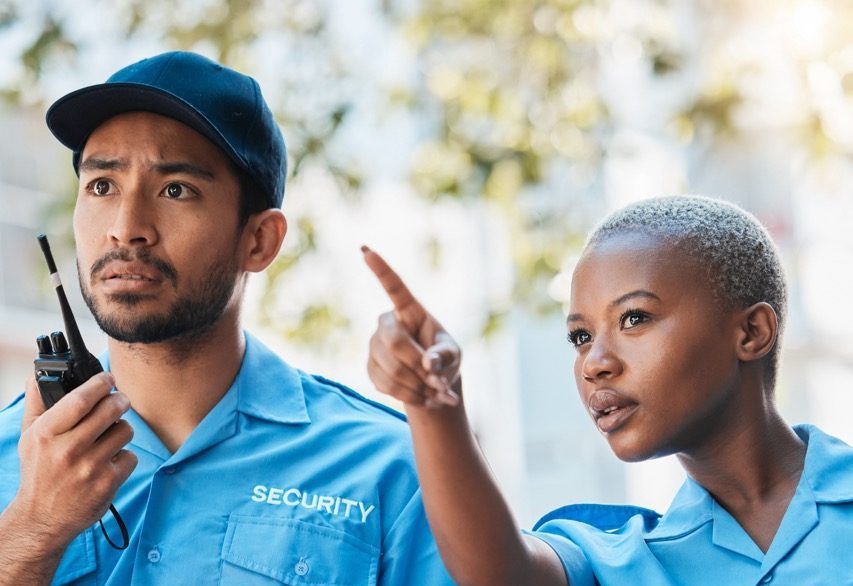 Two security guards responding to an incident while communicating by radio at an industrial facility. 