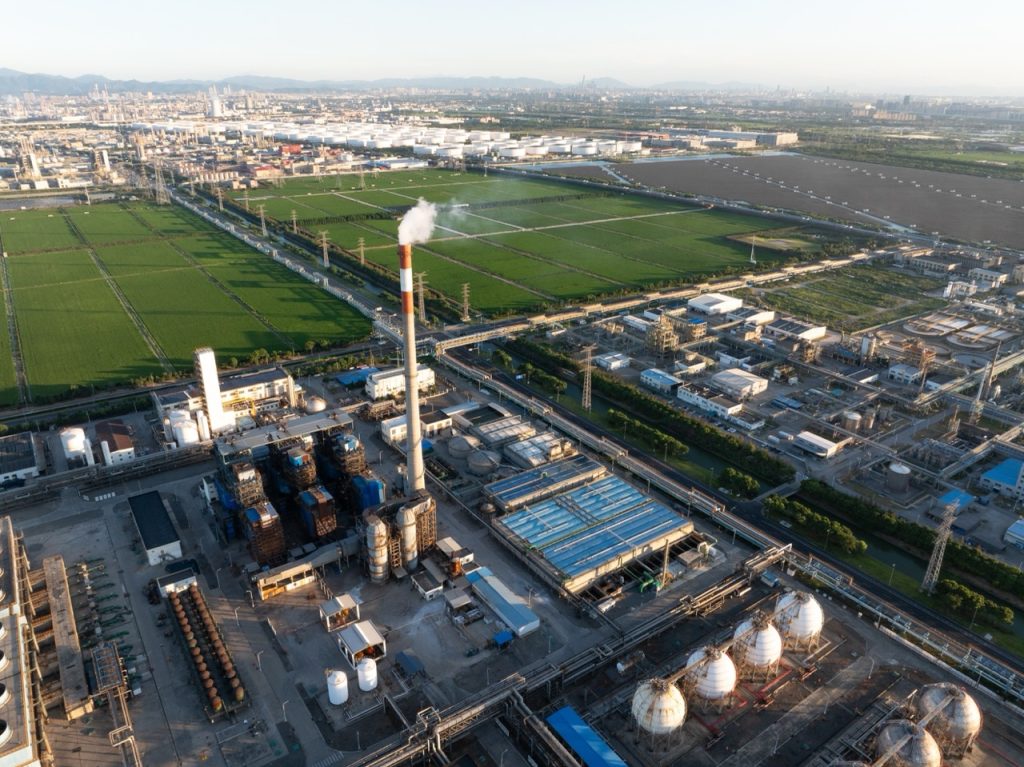Aerial view of sprawling chemical facility, featuring tall, narrow smokestack and multiple storage tanks and process units.