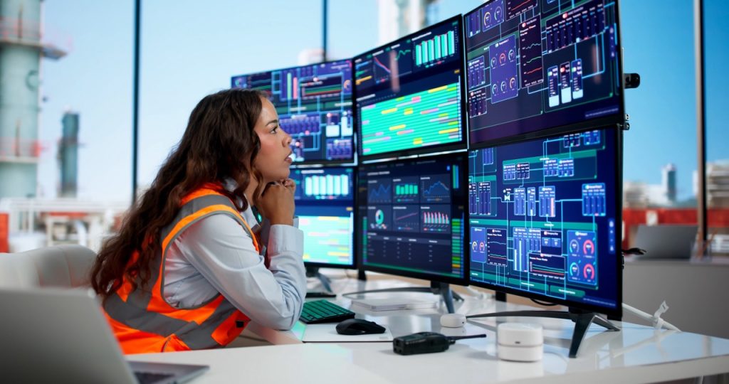 Chemical plant security operator studies six computer monitor screens full of notifications and alerts.