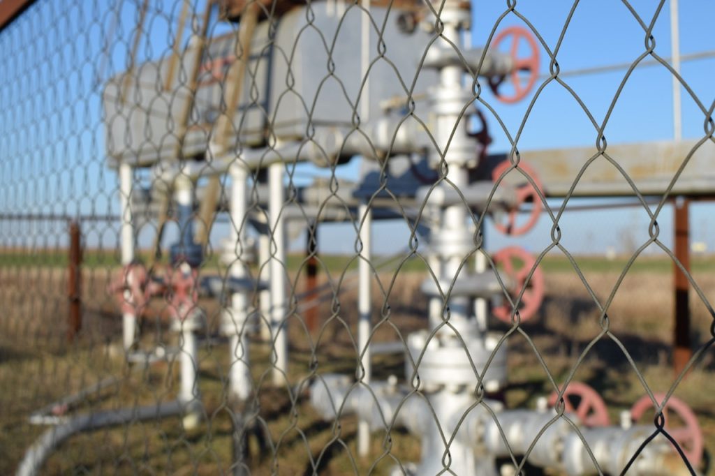 View of oil well valve shutoff assembly through chain link fencing.