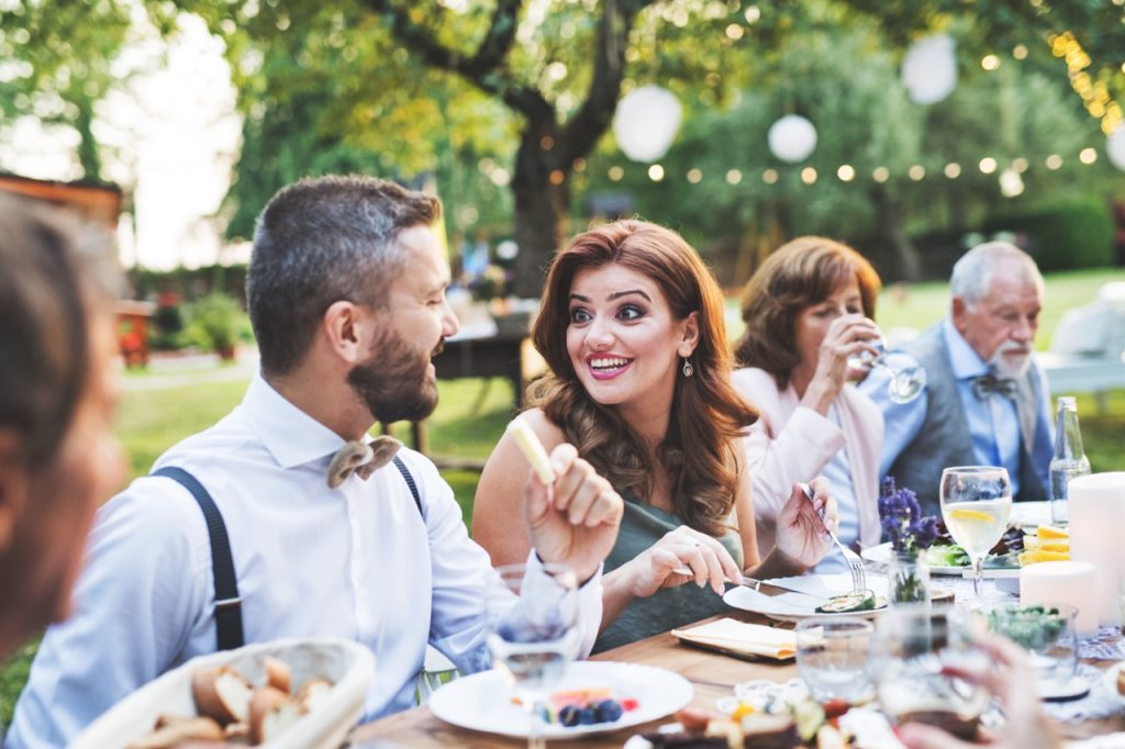 Guests eat and drink at an outdoor dinner gathering on the grounds of a private estate. 