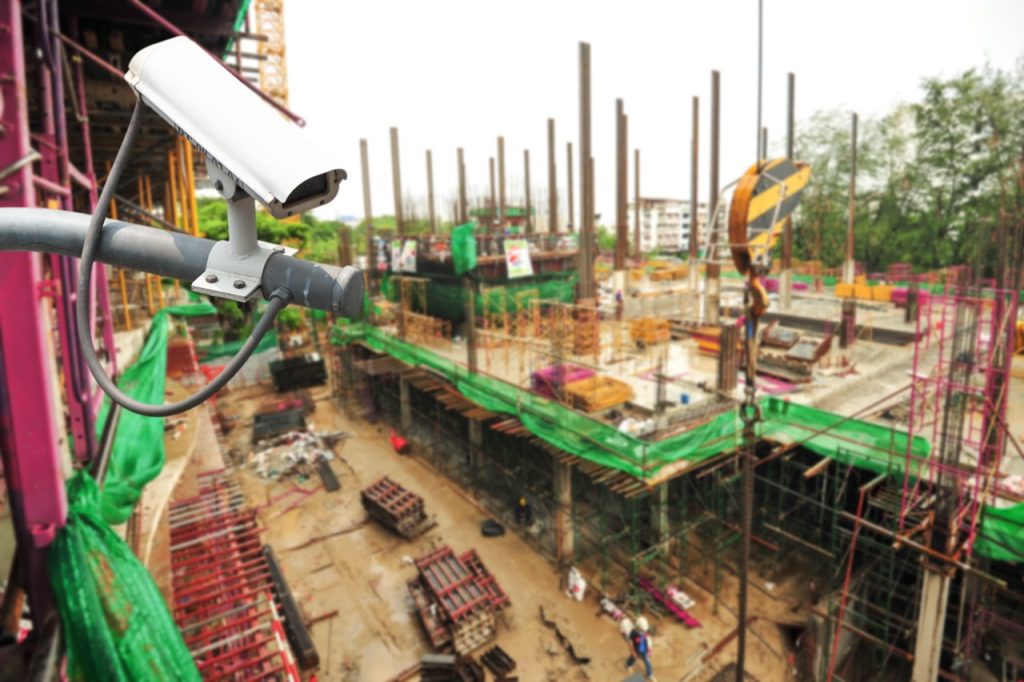Security camera overlooking an active construction site with building framework, materials, equipment, and workers. 