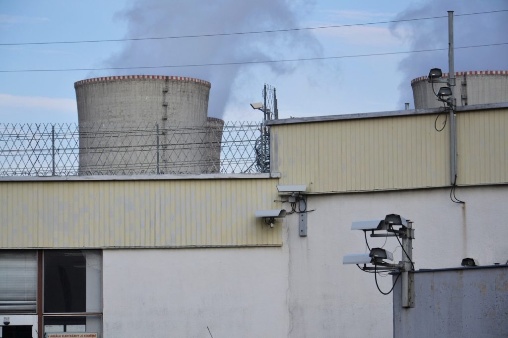 Security cameras mounted along the perimeter of an energy facility with cooling towers visible in the background. 