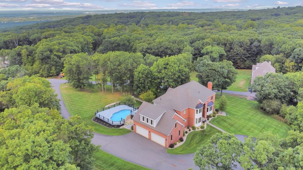 Aerial view of a private estate with expansive wooded grounds, a gated drive, and a secluded main residence with pool.