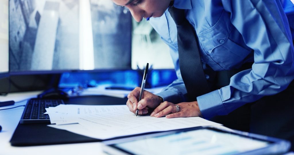 Security officer completing physical security records at a monitoring station. 