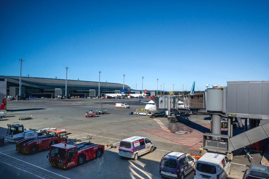 Airport apron with aircraft, jet bridges, and ground support vehicles inside a secured airport operations area. 