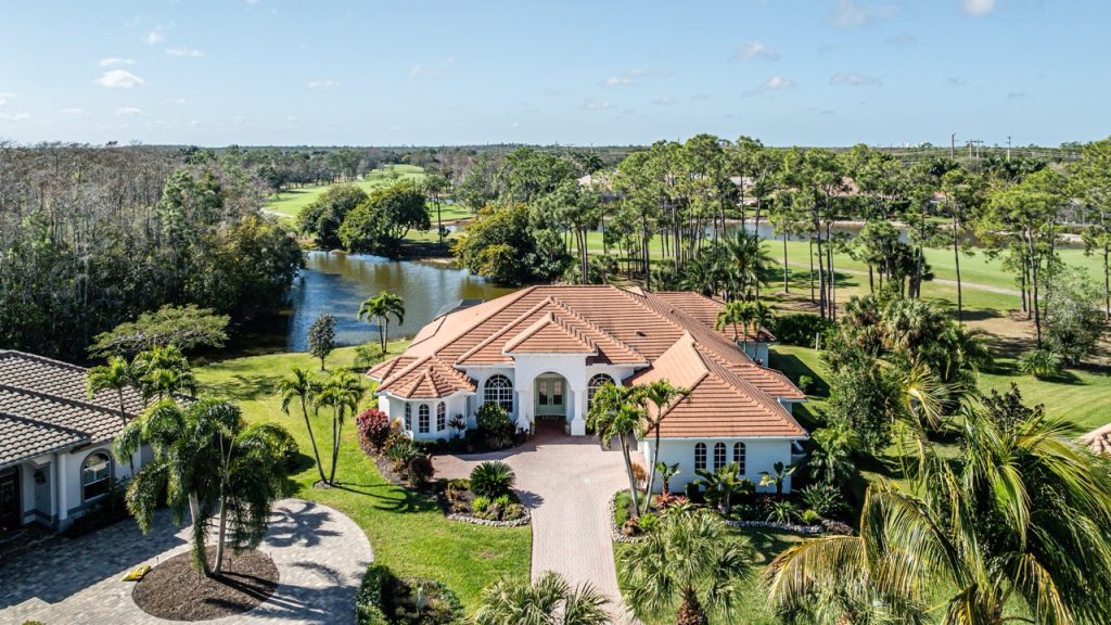 Aerial view of a waterfront private estate with landscaped grounds, mature trees, and surrounding open green space.