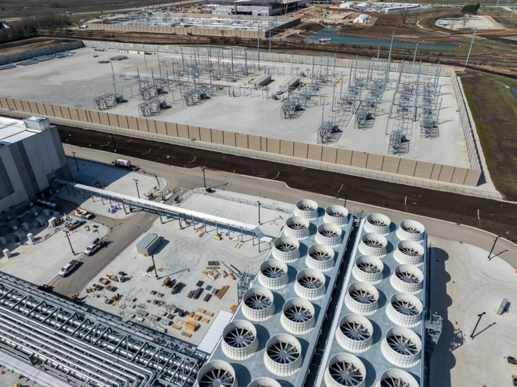 Aerial view of data center campus with cooling systems, power substation, and secured utility infrastructure.