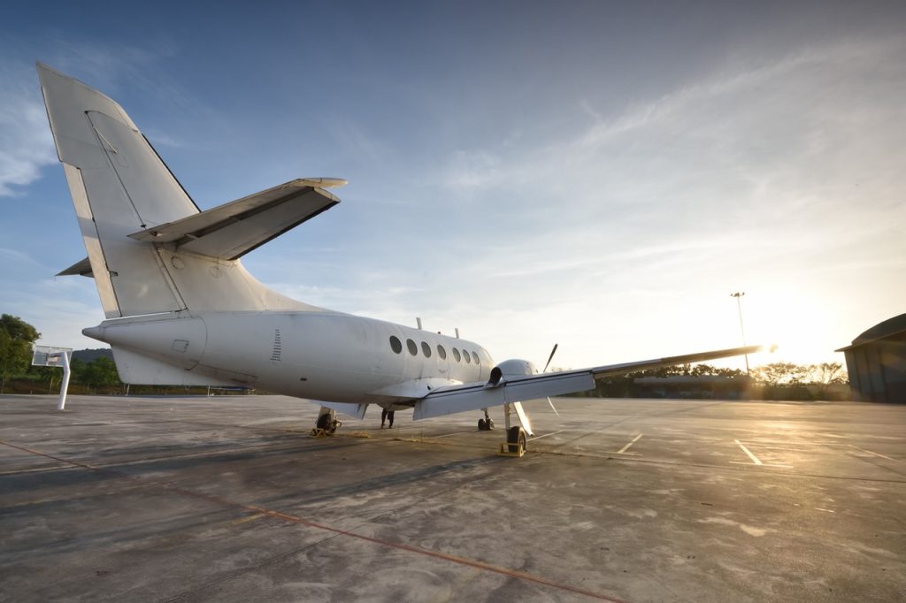 Aircraft parked on an airport apron near a maintenance hangar during sunset. 