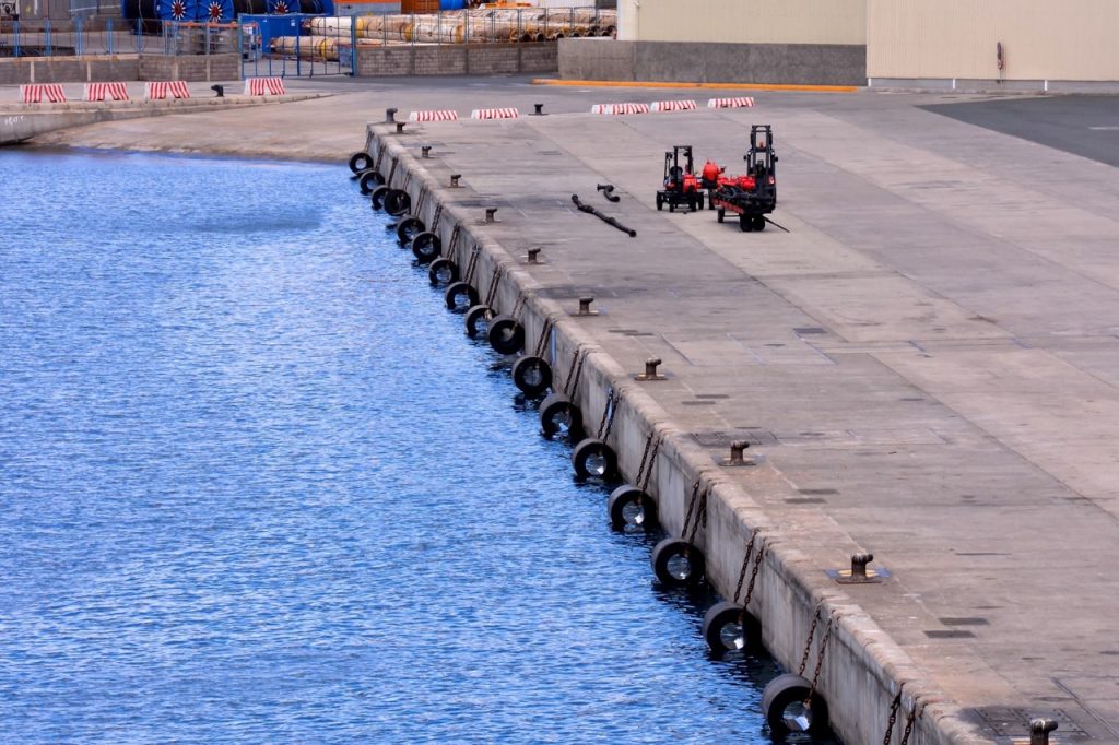 Waterside edge of a maritime terminal with an open quay, mooring bollards, and dock equipment beside the water.
