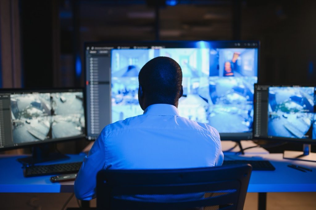 Maritime security operations center staff member monitors multiple surveillance camera feeds on large computer display screens.